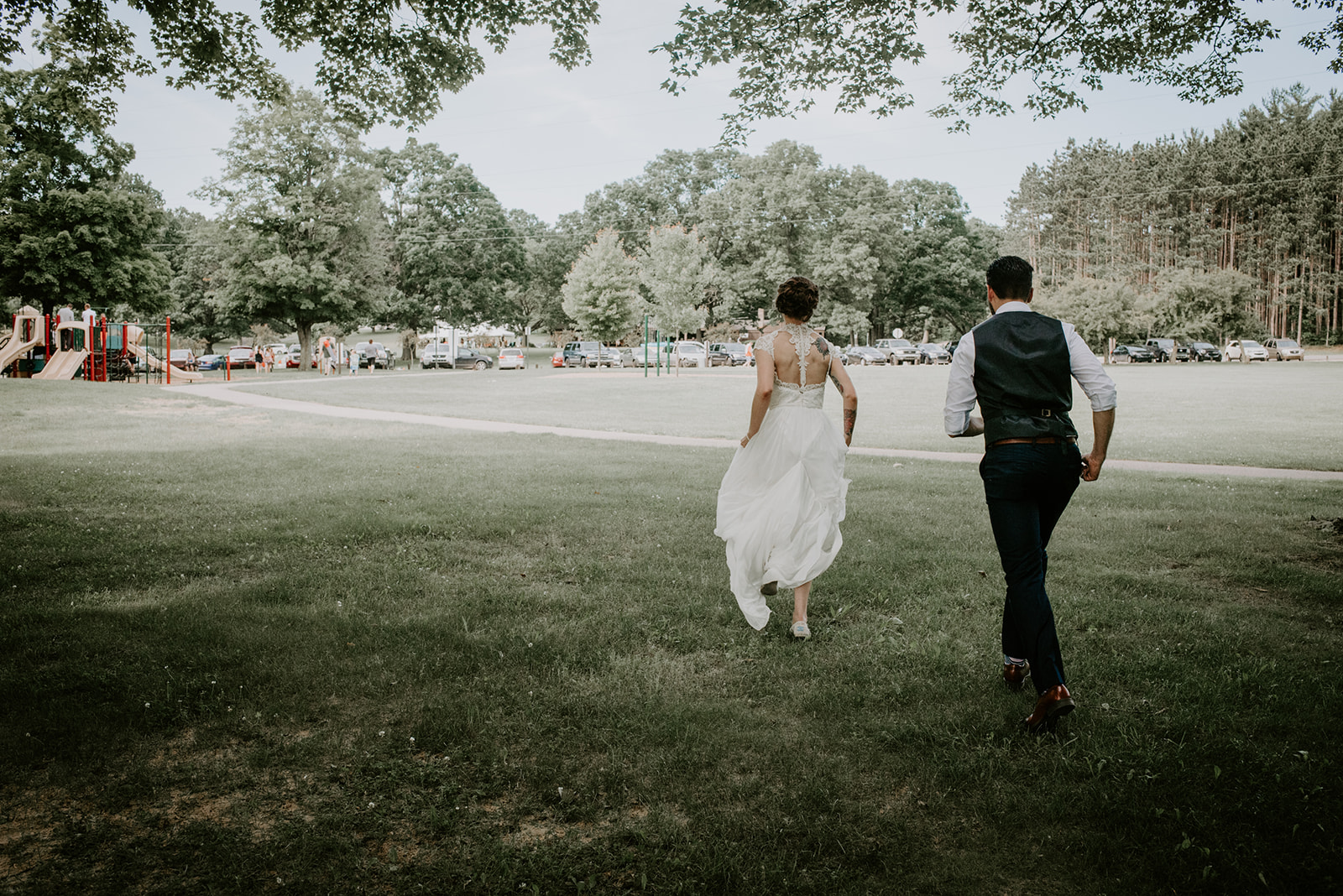 two marriers one in a white dress from Bianka Bridal and one in a blue suit running in Long Lake Park in Sparta Michigan on their wedding day
