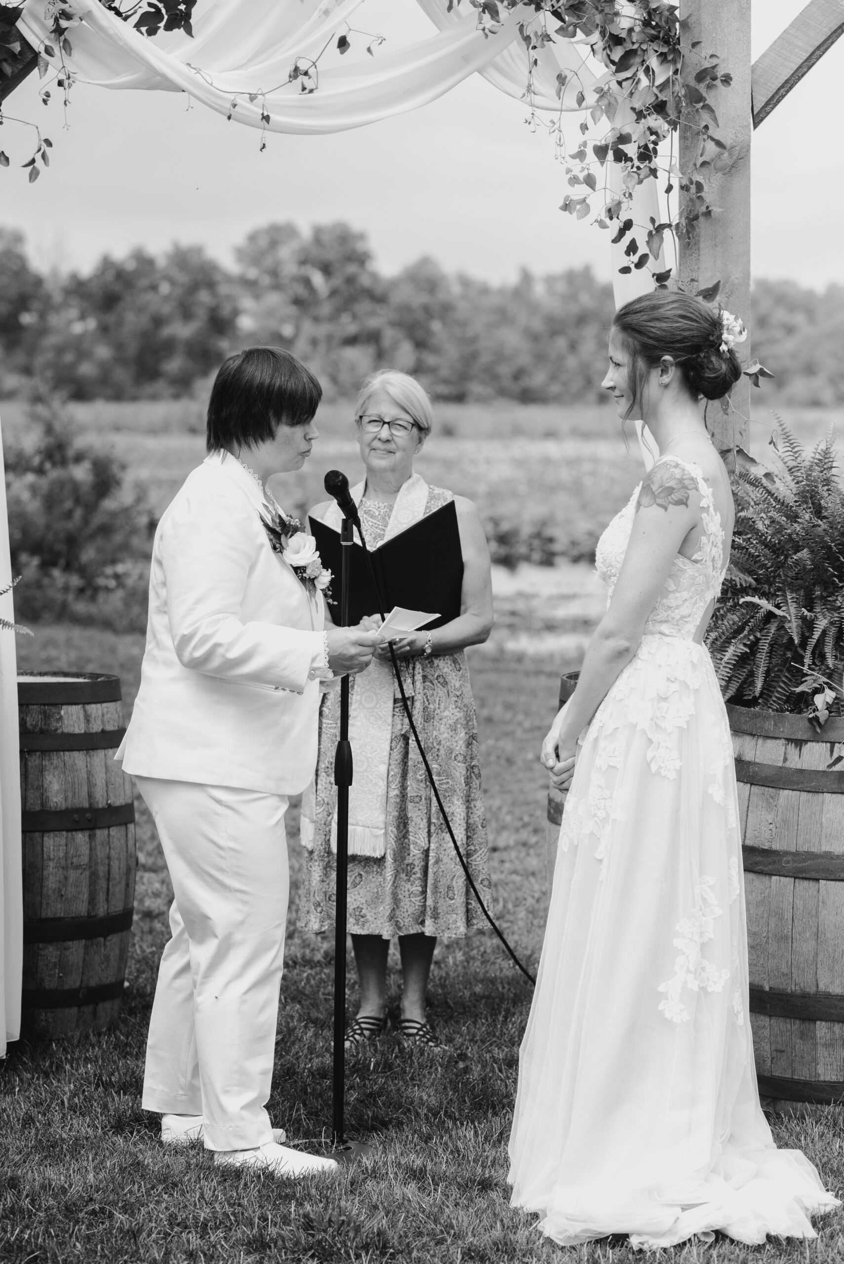 black and white image of two brides getting married during their backyard wedding ceremony one bride in j crew suit one bride in white wedding dress lgbtq wedding in lawton michigan photograped by queer wedding photographer Liv Lyszyk Photography