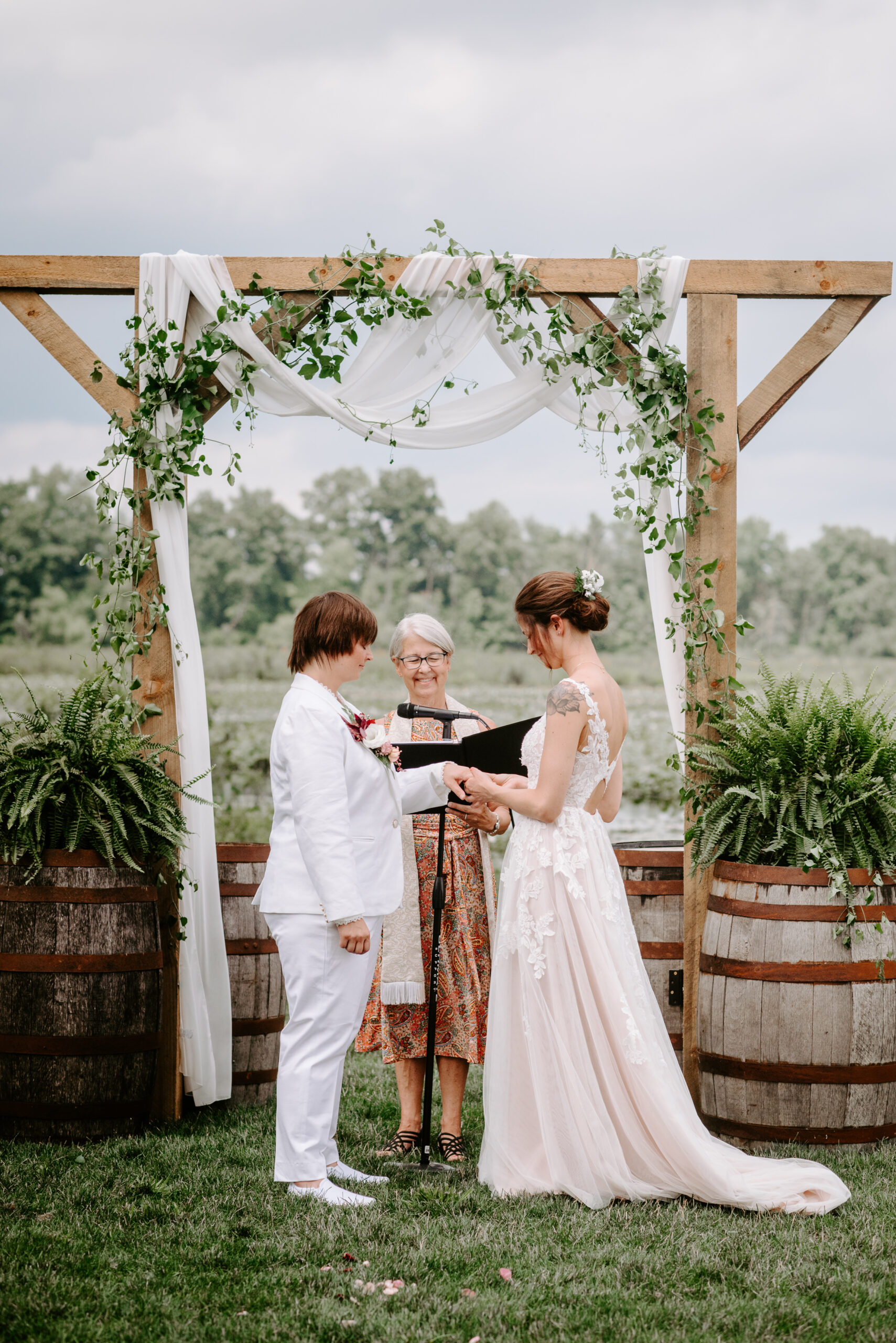 image of two brides getting married during their backyard wedding ceremony one bride in j crew suit one bride in white wedding dress lgbtq wedding in lawton michigan photograped by queer wedding photographer Liv Lyszyk Photography