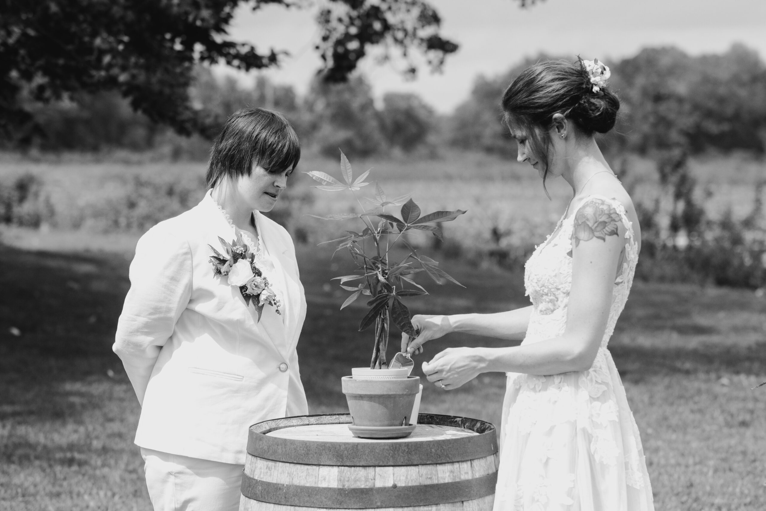 black and white image of two brides in backyard LGBTQ wedding in Lawton Michigan potting a small tree during unity ceremony photography by queer wedding photographer Liv Lyszyk Photography