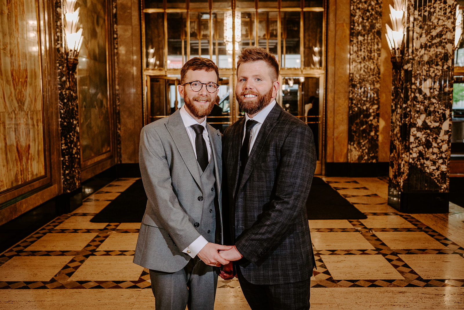 two gay men in gray and black suits on their wedding day having their photos taken at the historic fisher building in downtown detroit by Liv Lyszyk photography a queer and non binary wedding photographer from Grand Rapids Michigan