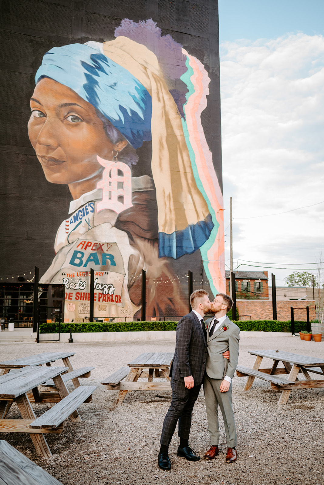 Formal portrait of two gay grooms featuring the girl with the detroit earring mural painted outside of chroma detroit in michigan an elegant black tie wedding captured by Liv Lyszyk Photography a queer wedding photographer based out of Grand Rapids Michigan
