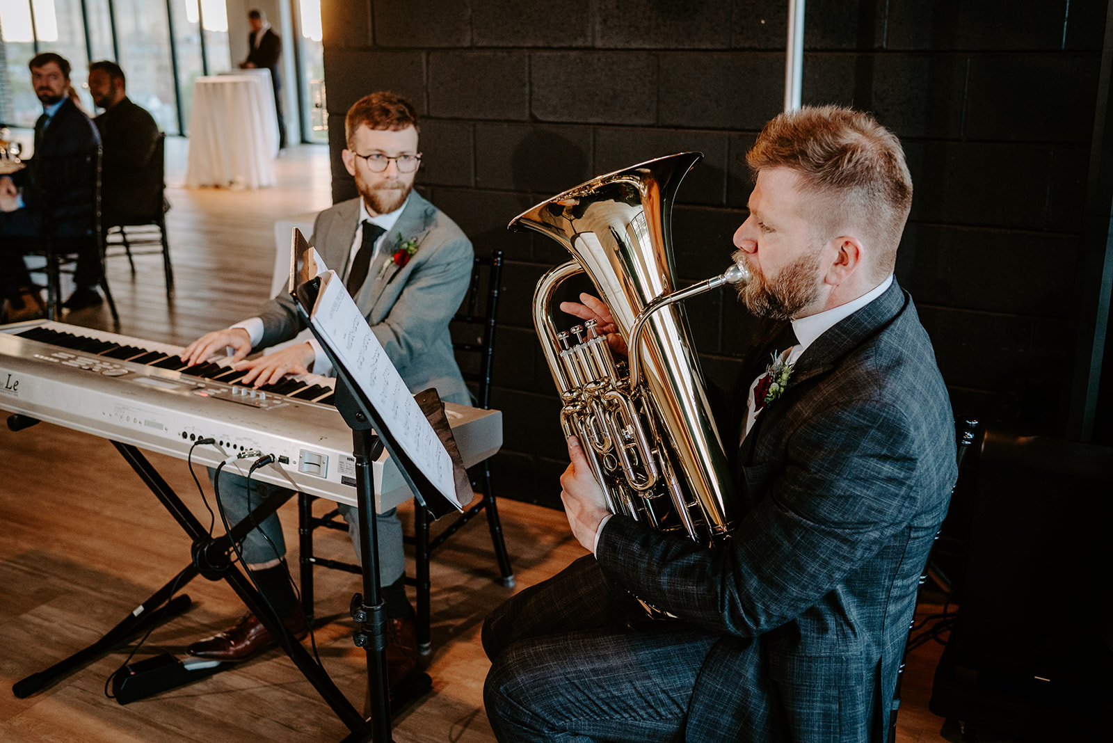 two grooms playing euphonium and piano at the beginning of their reception on the top floor of chroma events in downtown detroit captured by queer wedding photographer Liv Lyszyk Photography