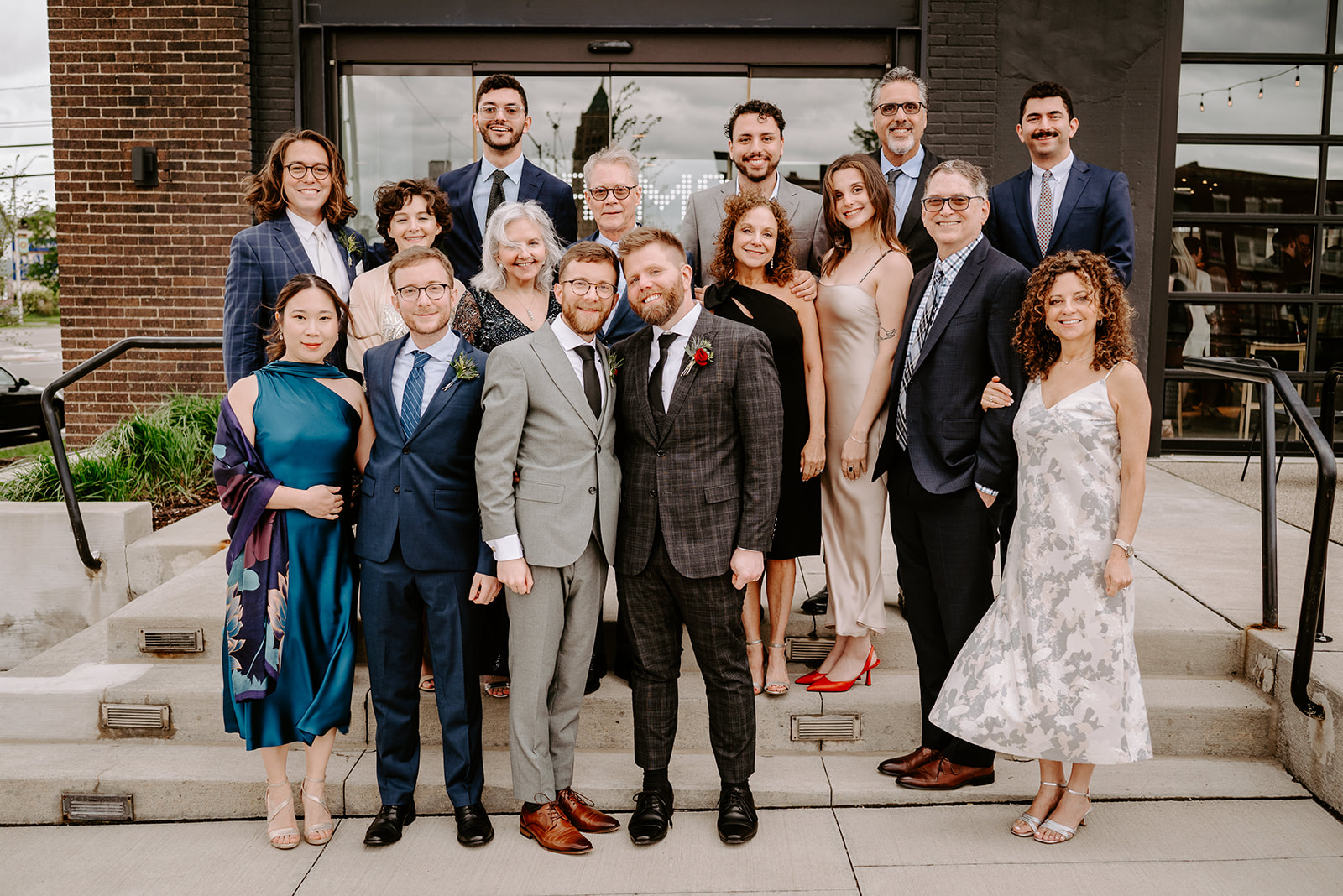two gay grooms in black and gray suits with their families outside of chroma detroit in michigan an elegant black tie wedding captured by Liv Lyszyk Photography a queer wedding photographer based out of Grand Rapids Michigan