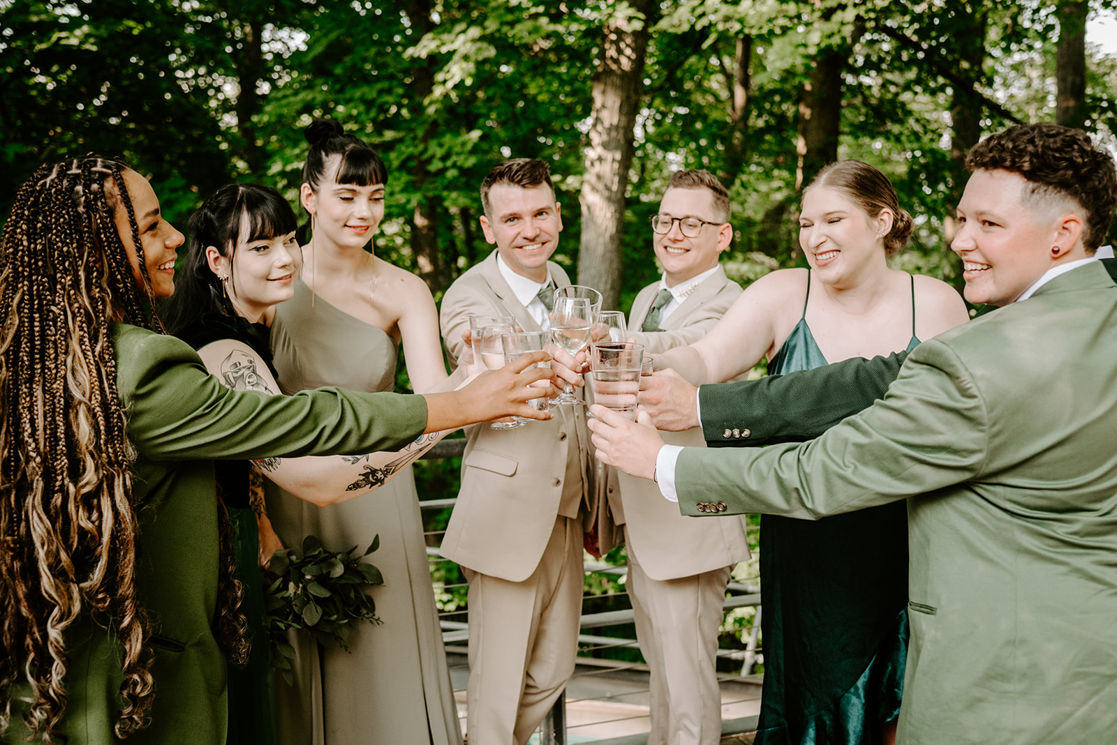 lgbt boho neutral wedding at john ball zoo in grand rapids michigan two grooms in tan suits with green accents with wedding party in mismatched green attire clinking champagne glasses in semi circle