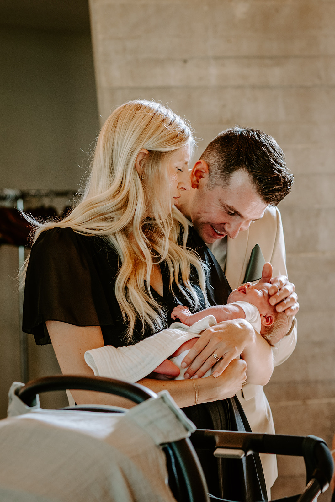 lgbt boho neutral wedding at john ball zoo in grand rapids michigan groom in tan suit with green tie lovingly looking at newborn baby with blonde guest