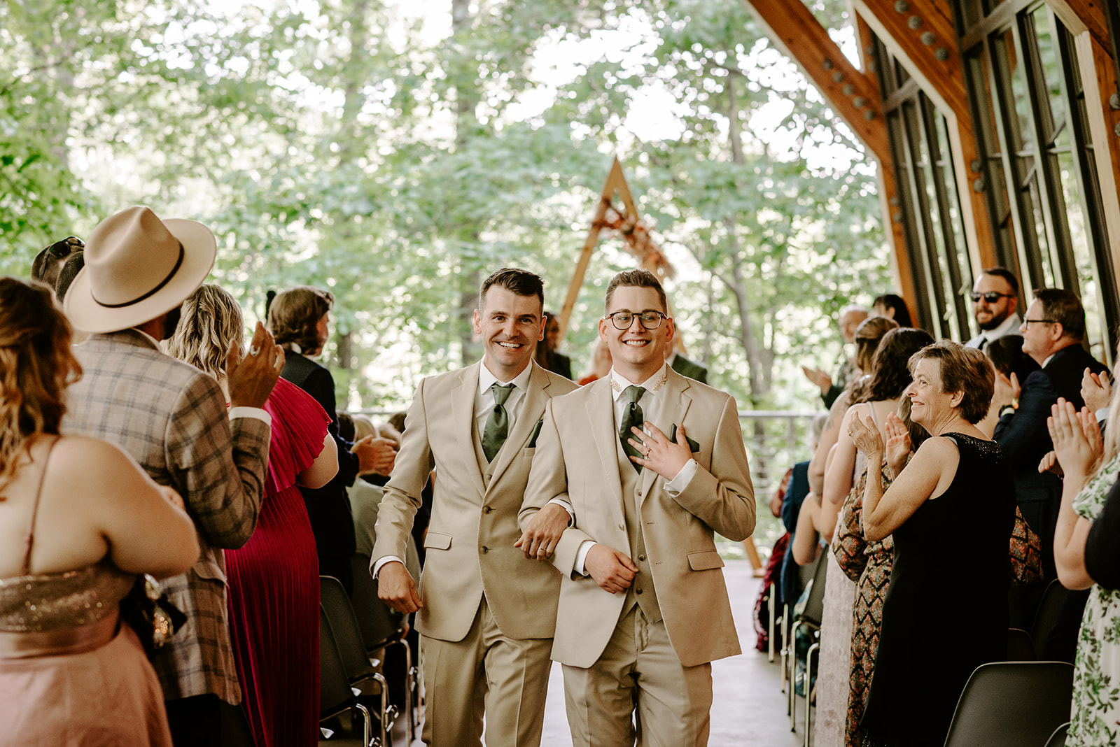 lgbt boho neutral wedding at john ball zoo in grand rapids michigan two grooms in tan suits with green accents walking back down aisle after saying I do with guests clapping