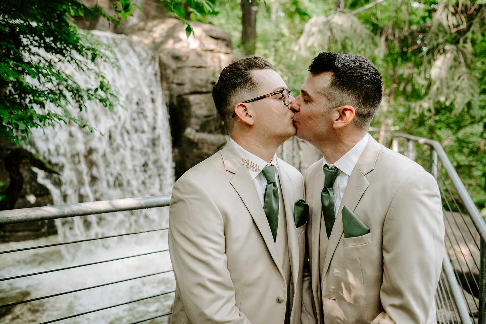 lgbt boho neutral wedding at john ball zoo in grand rapids michigan two grooms in tan suits with green accents kissing in front of waterfall