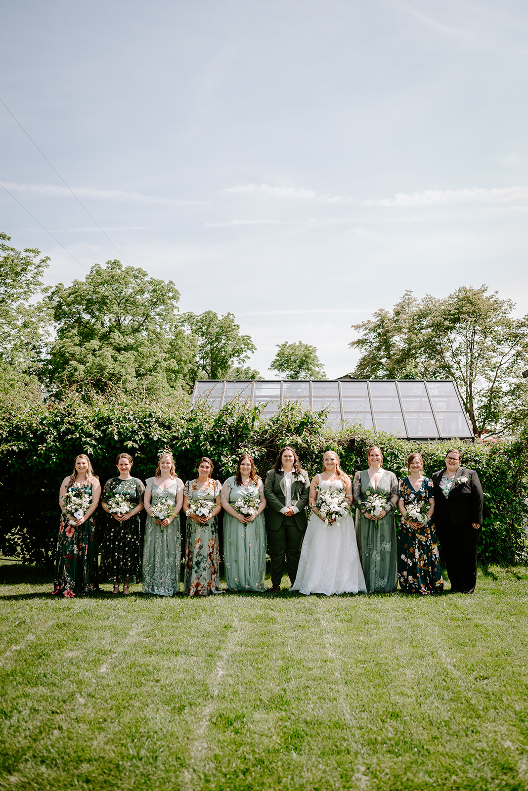michigan spring DIY lesbian wedding at black sheep shelter brides with wedding party in mismatch green floral dresses and outfits
