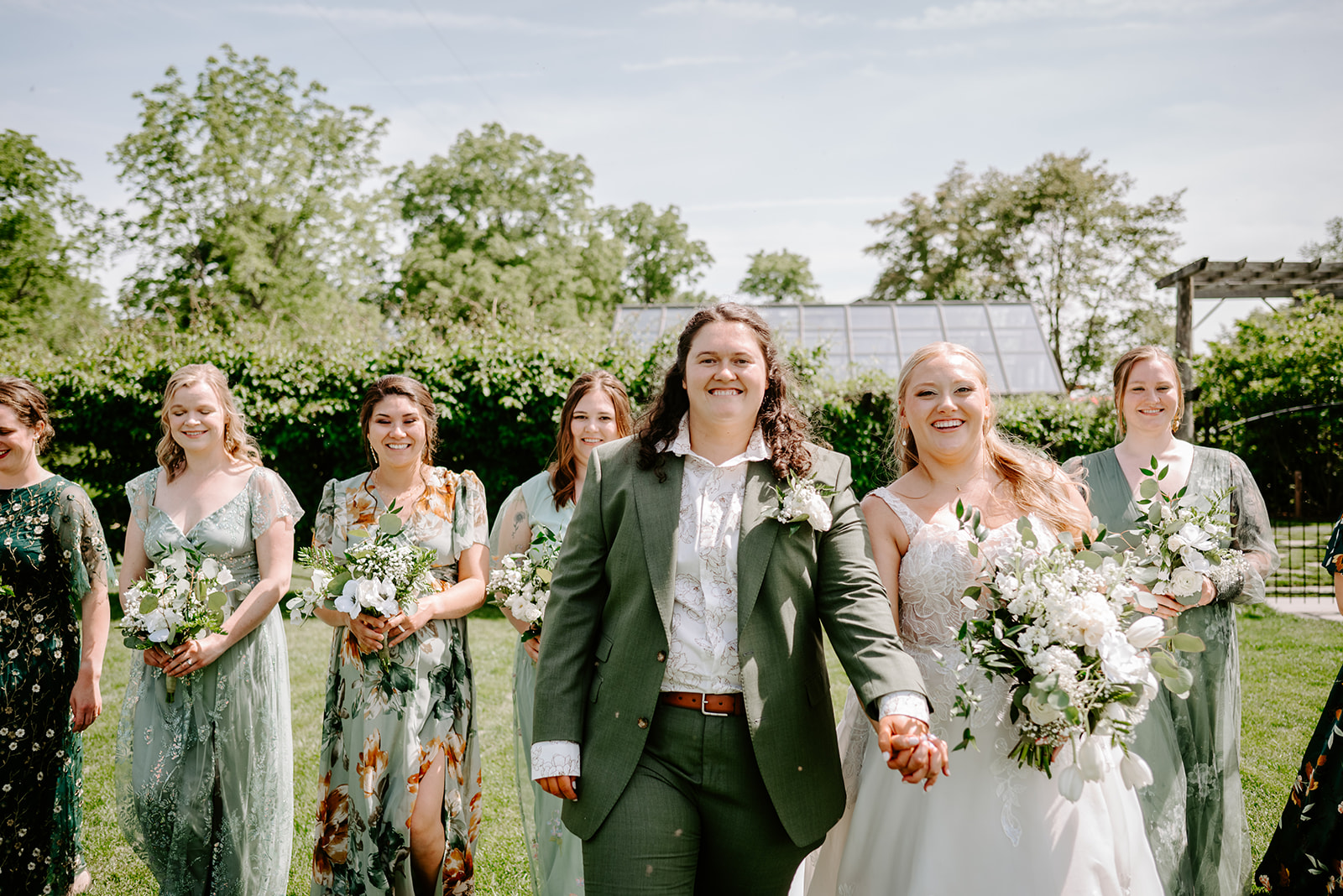michigan spring DIY lesbian wedding at black sheep shelter brides with wedding party in mismatch green floral dresses and outfits