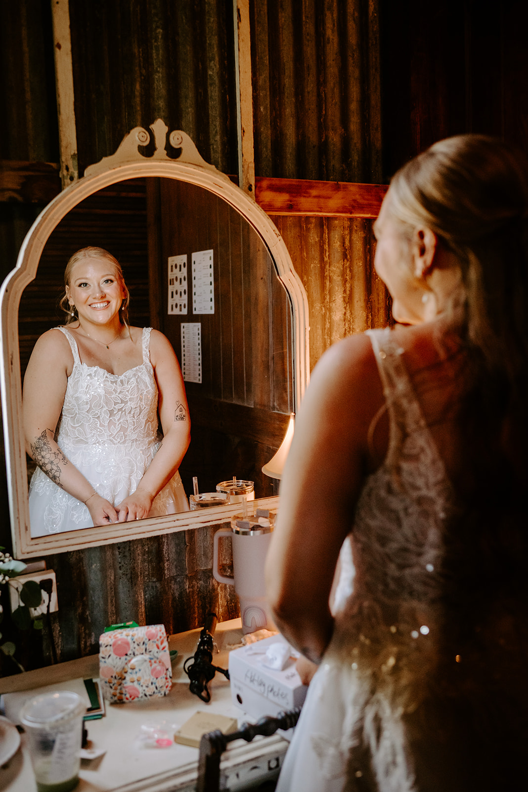 michigan spring DIY lesbian wedding at black sheep shelter bride looking into mirror while getting ready in her white dress with floral detailing
