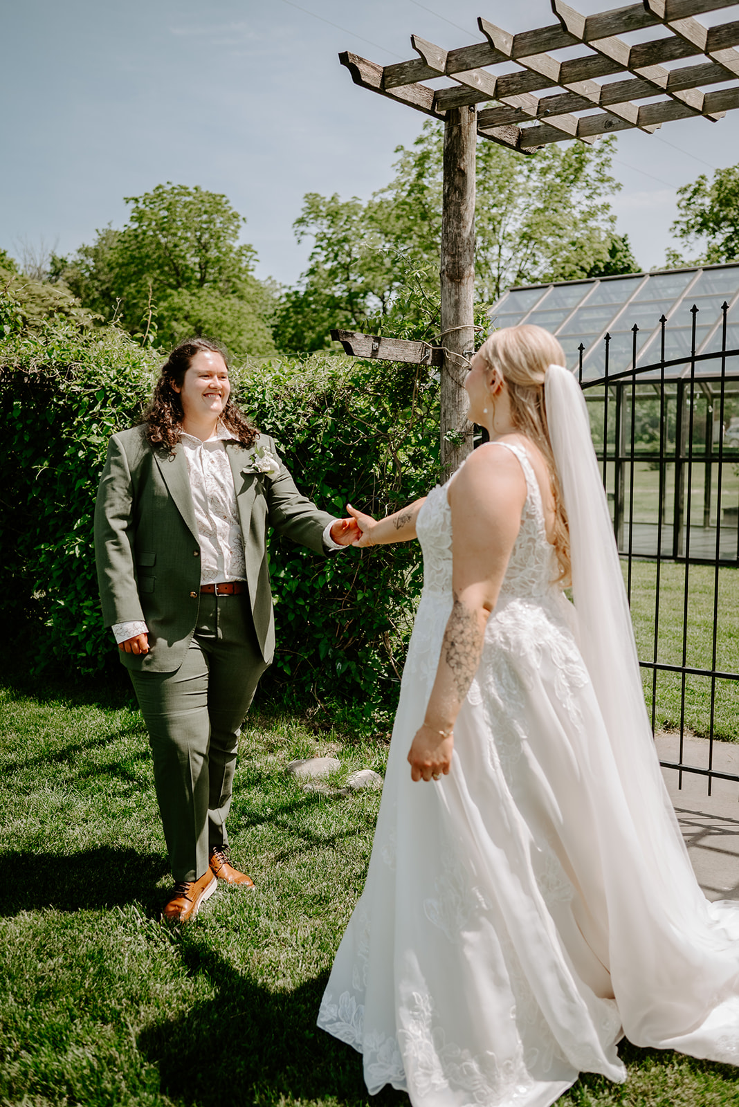 michigan spring DIY lesbian wedding at black sheep shelter two brides at first look in front of iron gate holding hands