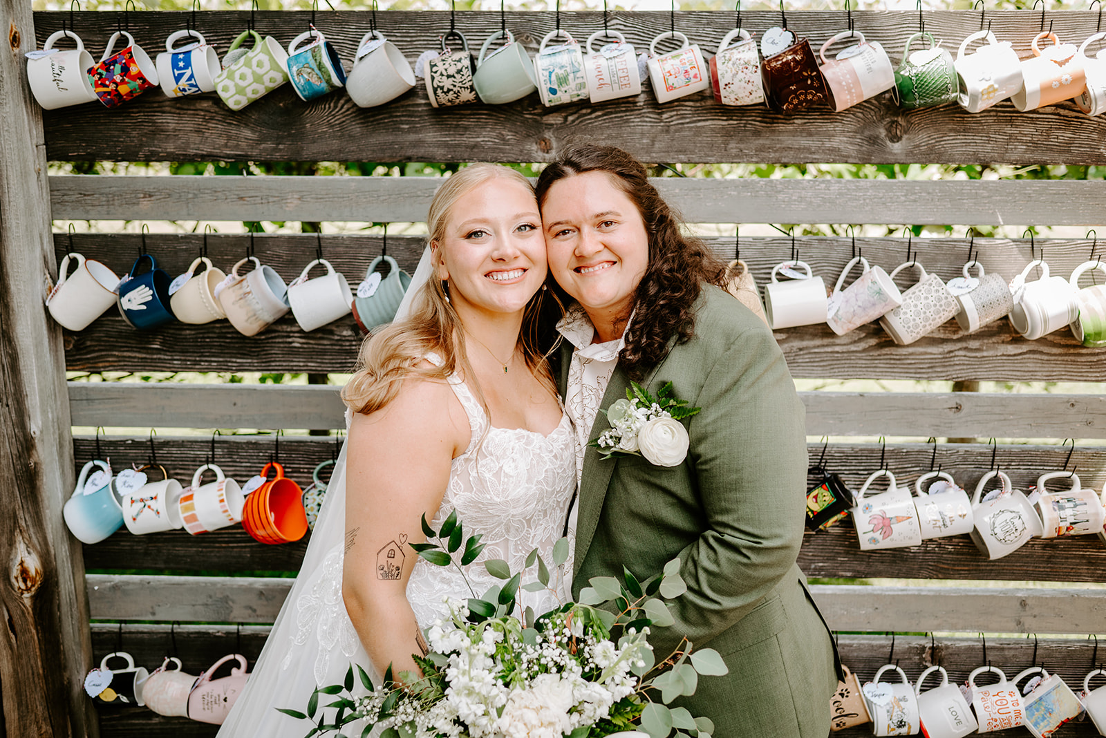 michigan spring DIY lesbian wedding at black sheep shelter in front of thrifted mug favor wall