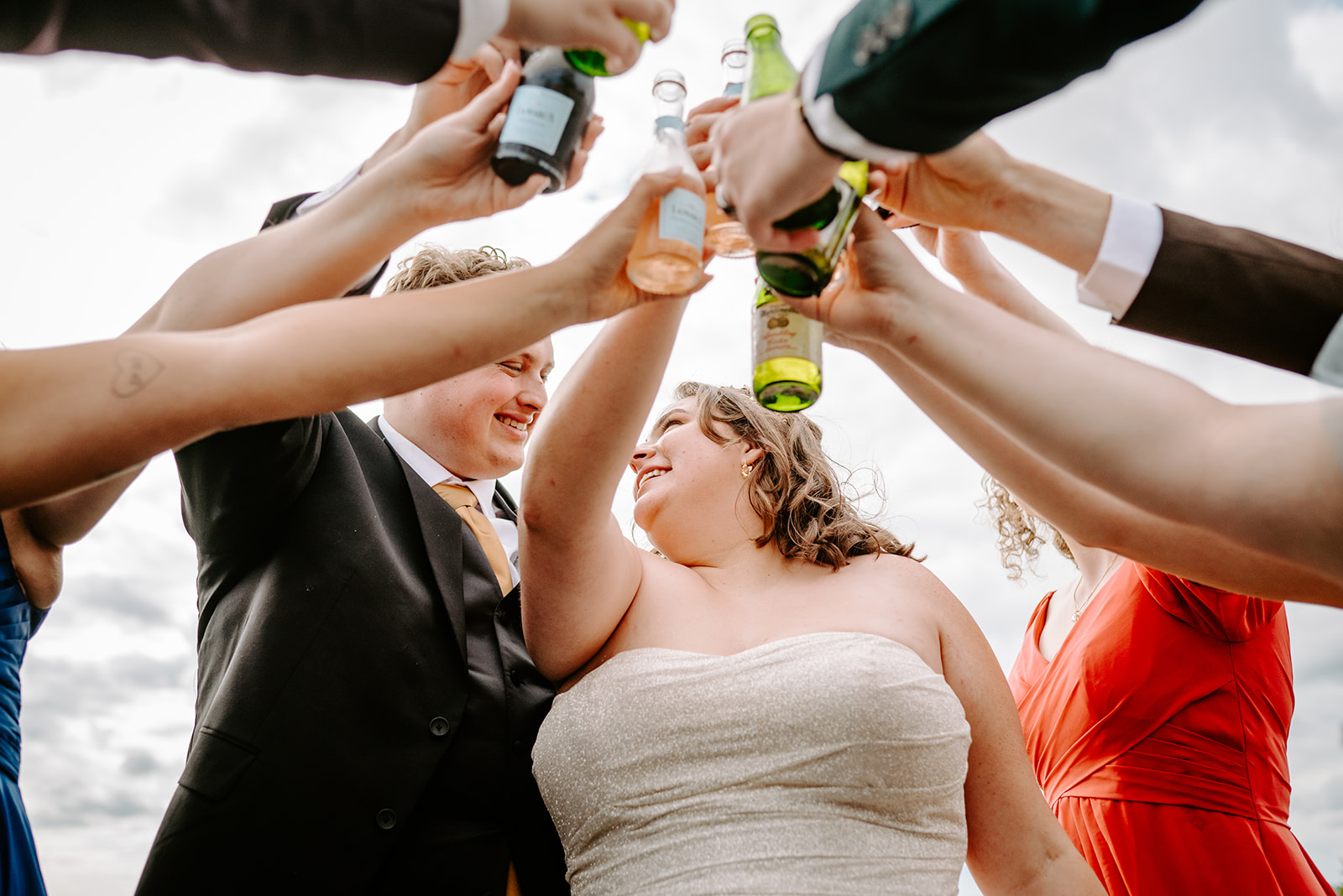 bride and groom with their attendants and wedding party clinking glasses and bottles after a colorful wedding in downtown grand rapids michigan
