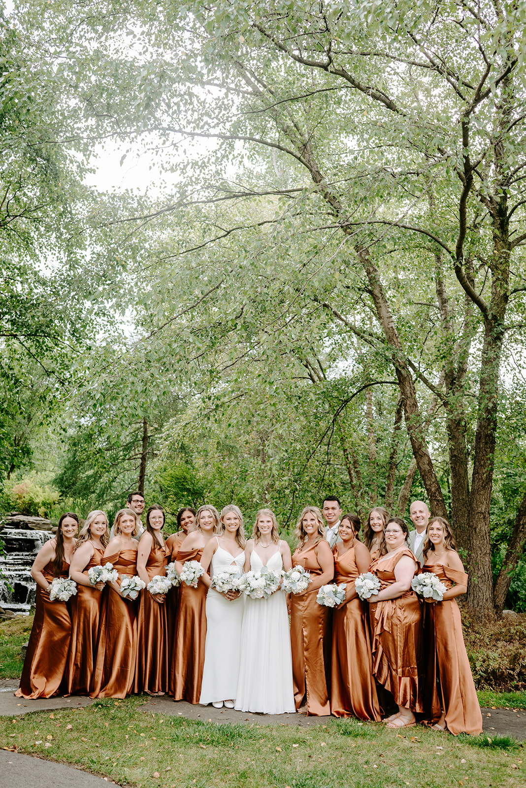 two brides getting married at Meijer gardens at a Grand Rapids LGBT Garden wedding with their wedding party in burnt orange silk gowns and floral bouquets